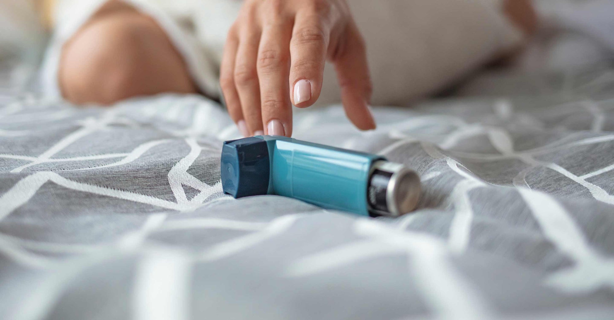 woman reaching for inhaler on bed