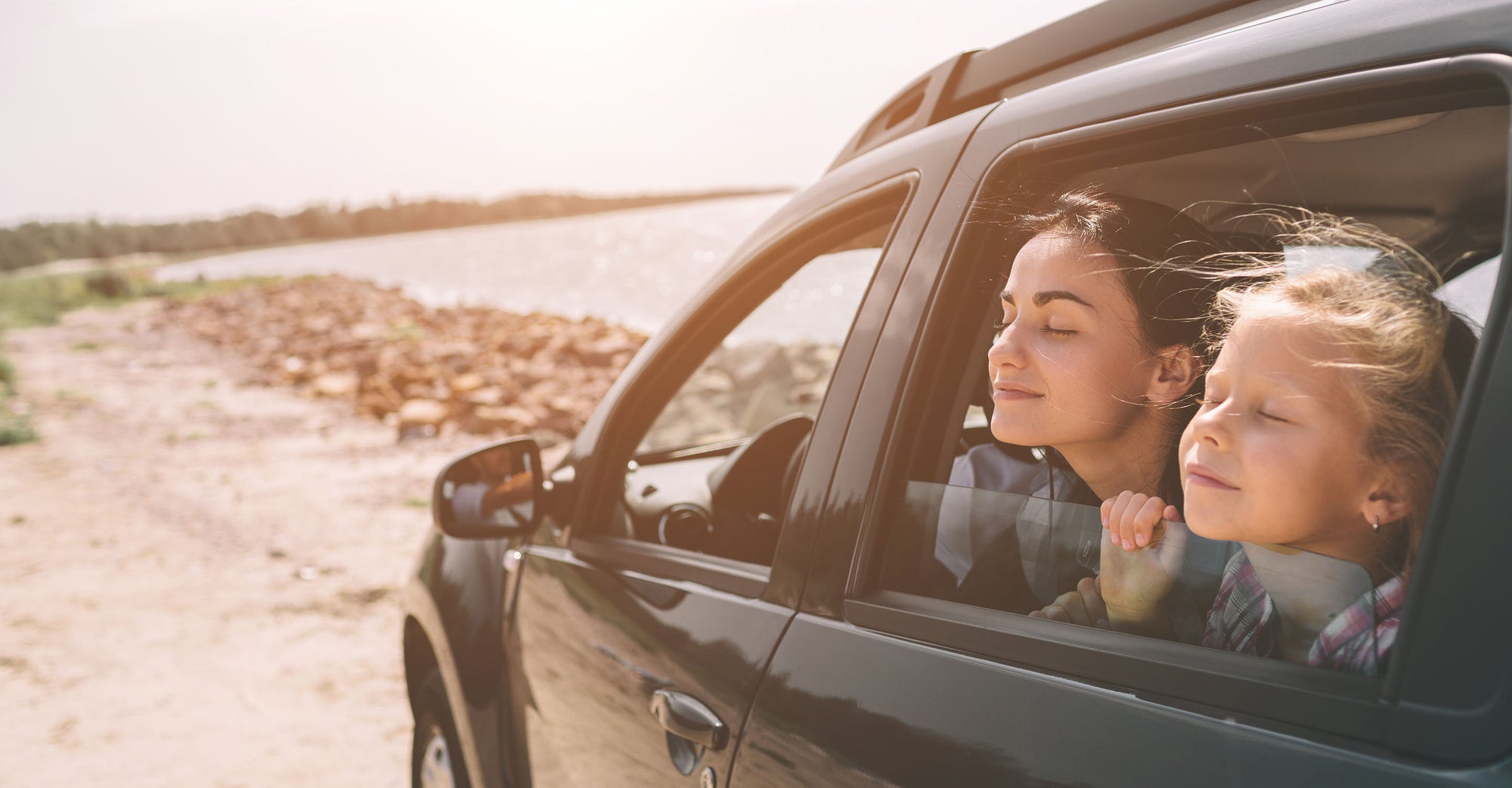 Mother and daughter breathing fresh air with window open during road trip