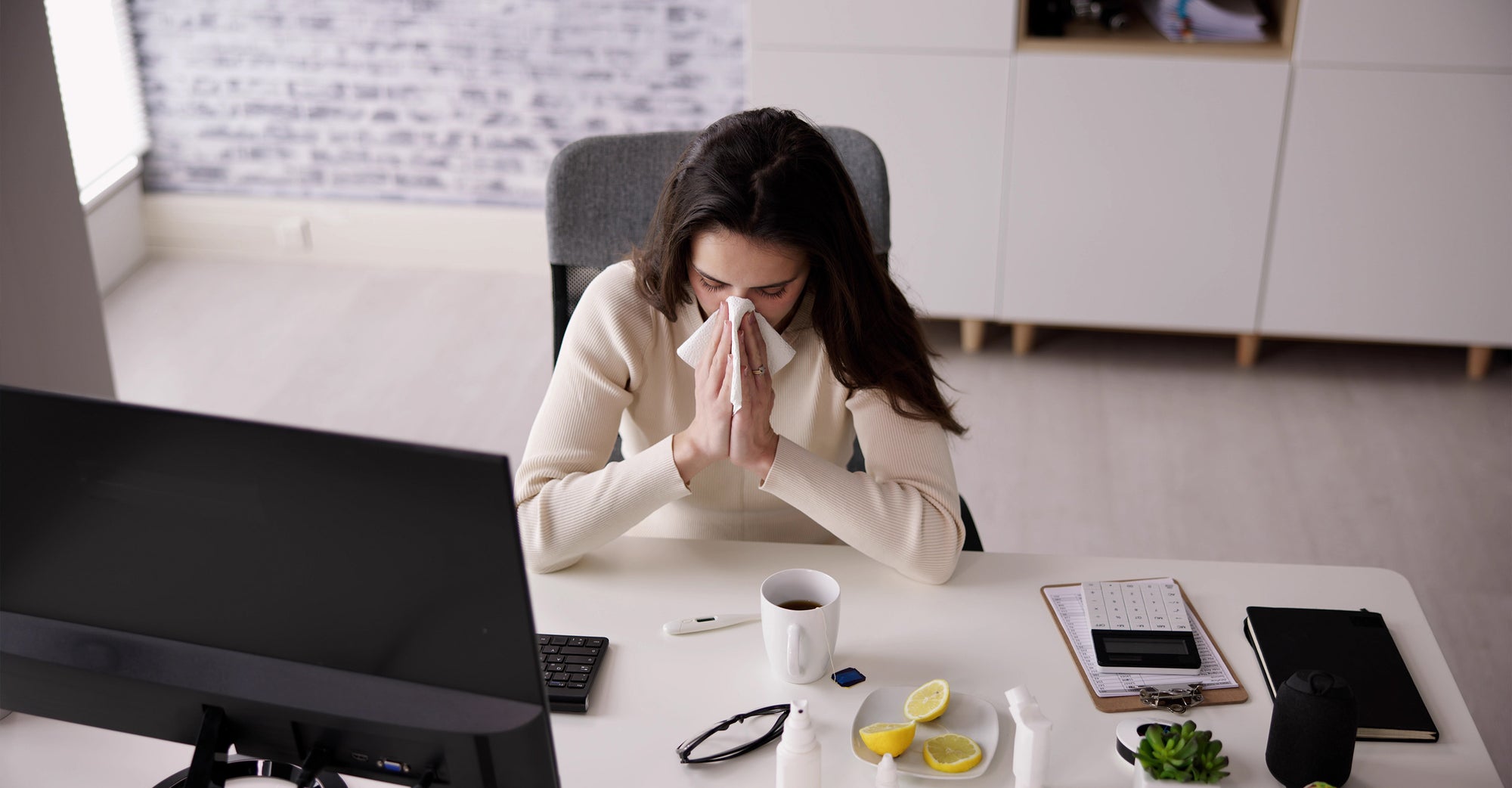 woman blowing nose at office desk